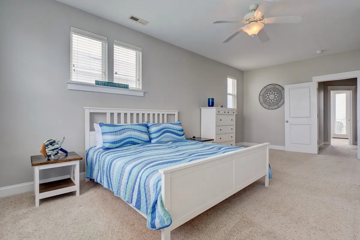 A serene bedroom featuring a king-sized bed with blue striped bedding, a nightstand with decorative items, and windows allowing natural light to flood the space, creating a tranquil atmosphere ideal for relaxation.