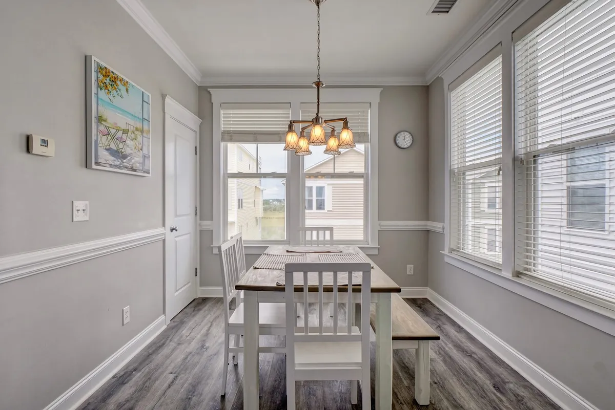 A warm, inviting dining area featuring a large table beneath a chandelier, with artwork on the wall and windows letting in natural light. The space is ideal for family meals, social gatherings, or enjoying a quiet coffee before heading out for the day.