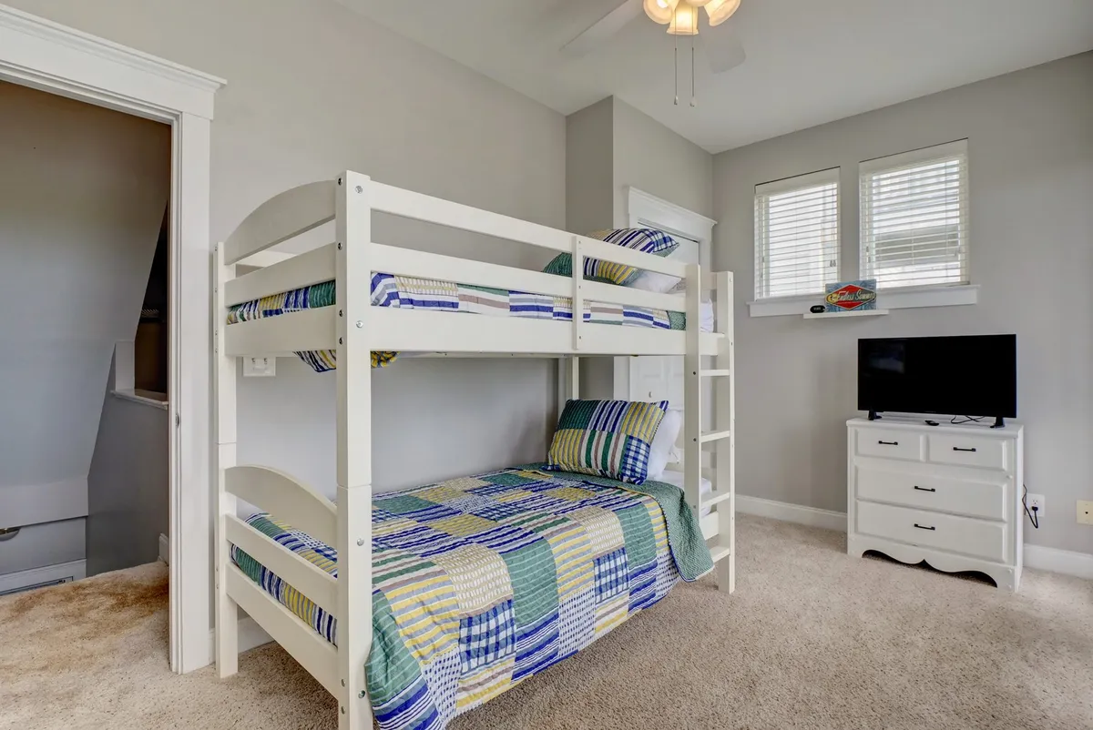 A playful bedroom featuring a twin-over-twin bunk bed with colorful bedding, complemented by a television and a compact dresser. The space is cheerful and designed with children in mind, offering room for play and relaxation.