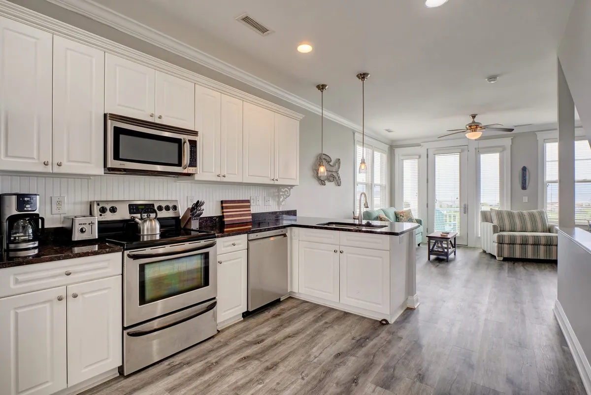This image spotlights the heart of the gathering level, with gleaming stainless-steel appliances, rich granite countertops, and an open layout that allows sunlight to pour in from generous windows. The living area in the background hints at the social, communal energy of the space, while the kitchen itself looks ready for both lively family feasts and casual brunches.