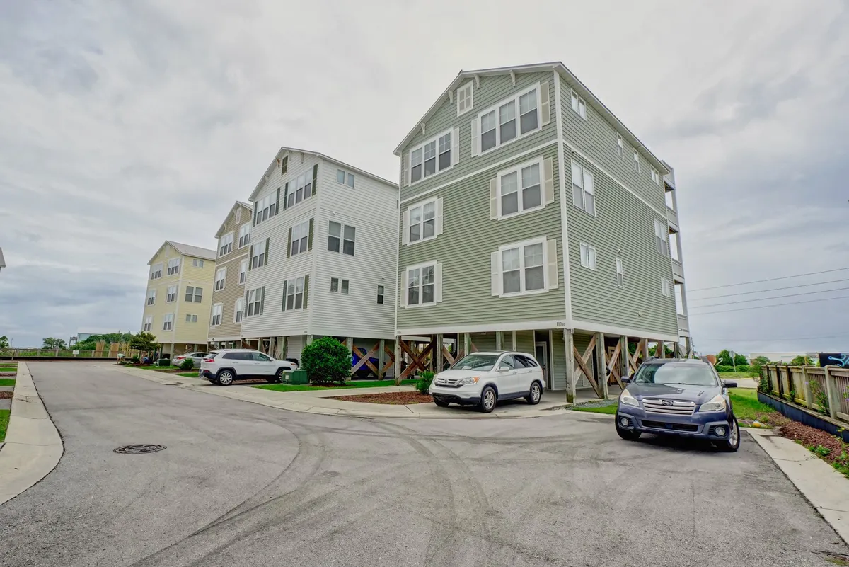 A welcoming exterior shot of modern multi-unit beach houses with green landscaping and cars in the driveway. The setting is friendly and relaxed, conveying the neighborhood's approachable atmosphere and the ease of returning home after an outing.