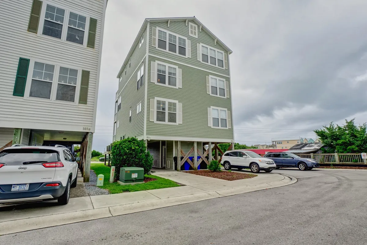 This image shows the exterior of the green house, with cars parked in front and a landscaped area that creates an inviting, homey atmosphere. The scene suggests a gathering place just steps from local attractions, with space for outdoor activities and easy access for multi-generational families or groups arriving together.