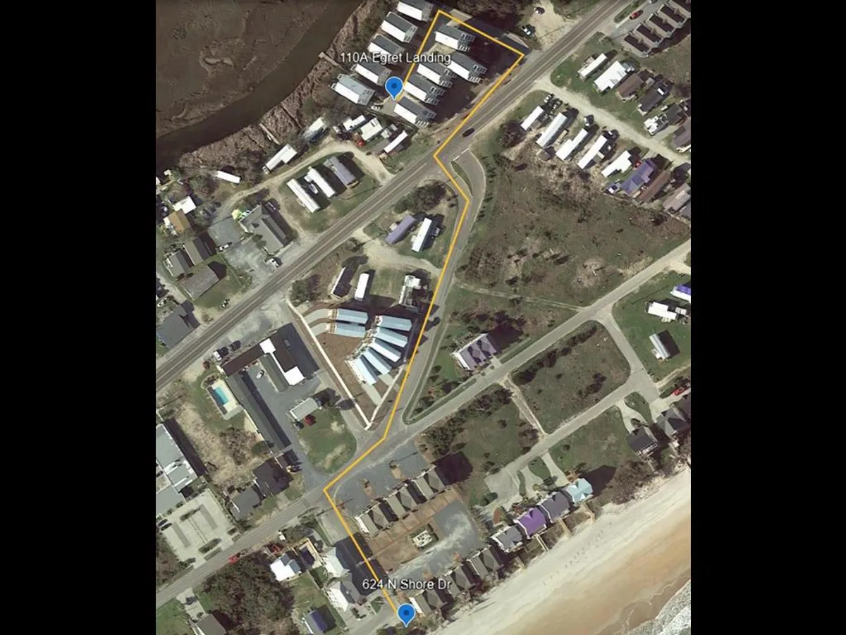 An inviting view encompassing the property's location (110A Egret Landing, 624 N Shore Dr) and the nearby beach area, with people walking and biking along coastal trails. The scene glows with the warmth of sunset, hinting at both the ease of beach access and the opportunities for exploring nearby attractions.