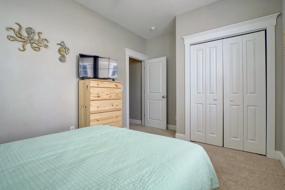 A spacious laundry room equipped with a wooden dresser, bed with mint green blanket partially visible, and decorative wall art. The area is functional and welcoming, suggesting space for laundry needs after sandy beach outings.