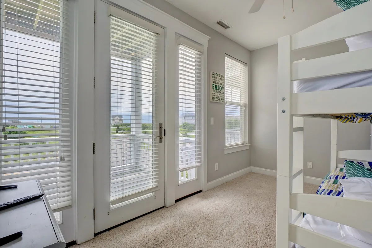 A bright and cozy bunk room with large windows, soft carpeted flooring, and a view out to the balcony. The space feels lively and inviting, perfect for relaxing, enjoying a book, or watching the sunset.