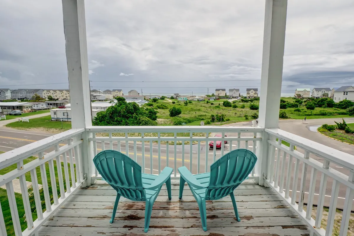A tranquil deck furnished with turquoise chairs overlooking a sweeping ocean view, with lush greenery and a cloudy sky, suggesting peaceful moments and breathtaking vistas from above.