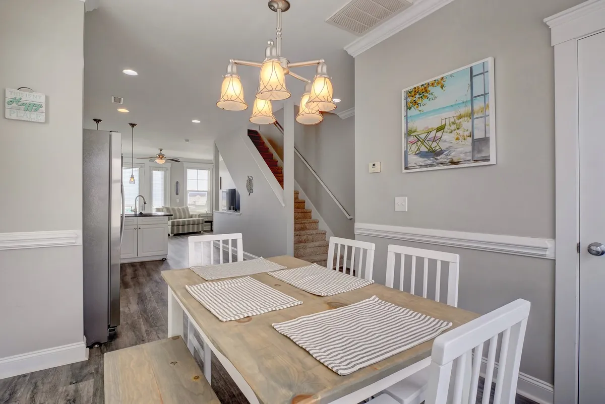 This inviting dining room features a large table beneath a stylish chandelier, with a staircase and artwork adding visual interest and warmth. The scene is set for everything from lively family dinners to board game nights, emphasizing the communal aspect of the gathering level.